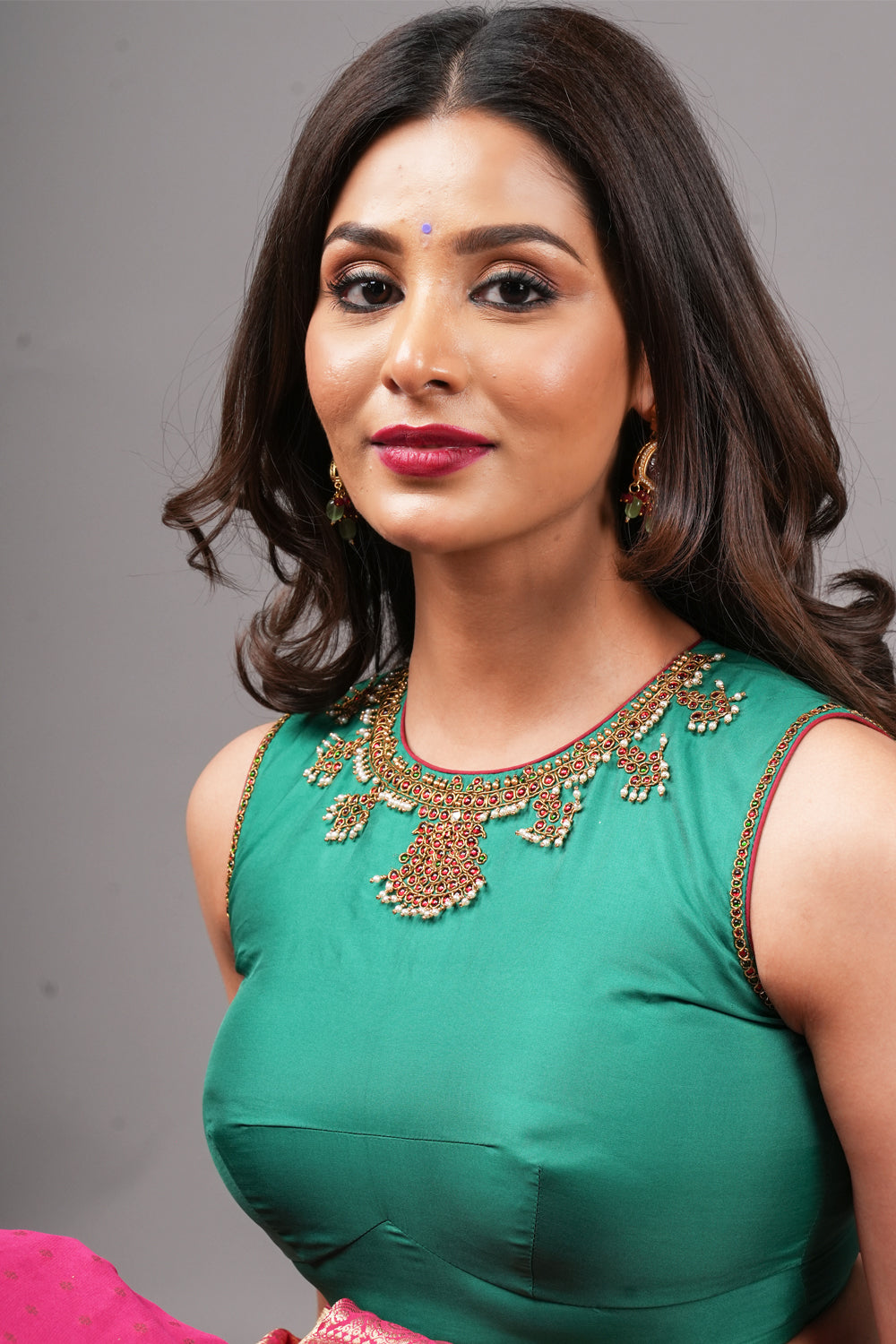 Emerald green silk close neck sleeveless blouse with hand embroidery around neck and armhole.